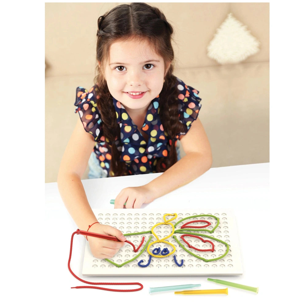 Quercetti Filo Filo arts and crafts scene featuring a young girl with braids creating a butterfly design on a white pegboard.