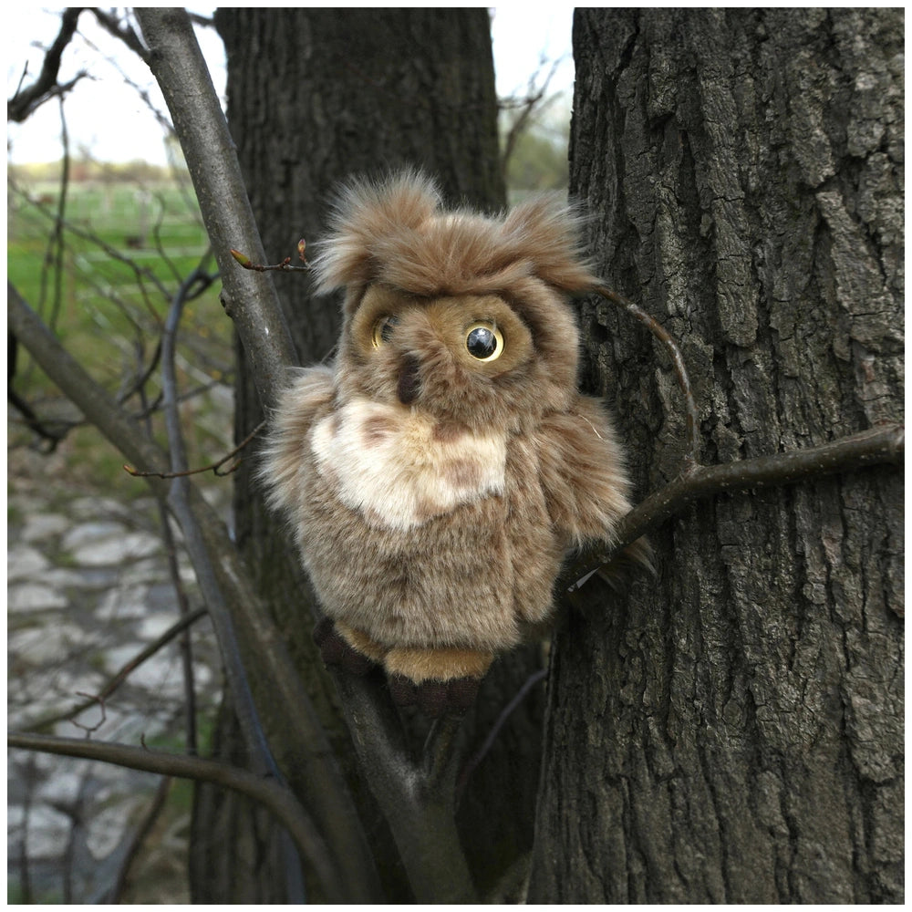 Plush eagle-owl toy with brown and white fur perched on a tree branch in a natural outdoor setting.
