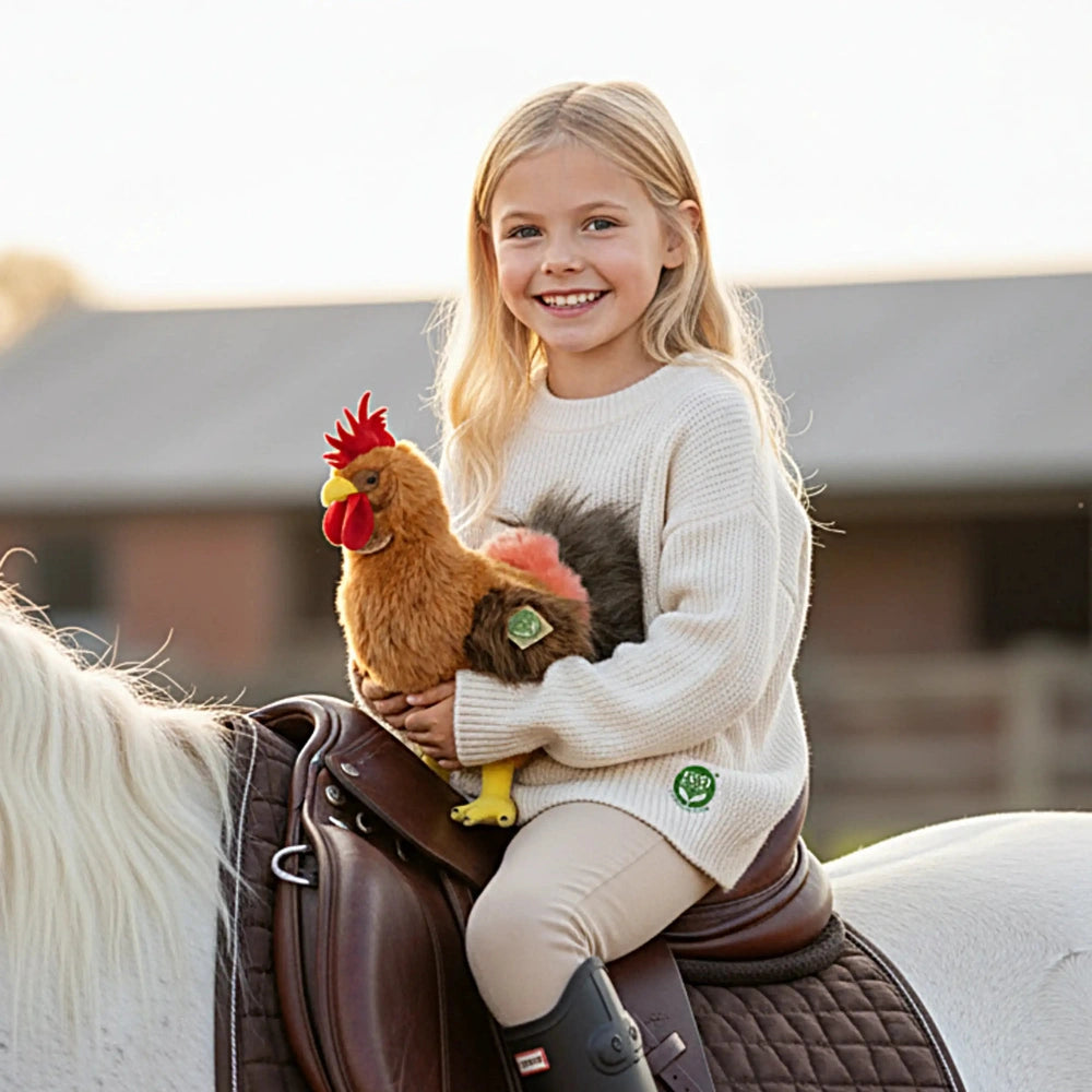 A young girl in a white sweater holds a red plush rooster while sitting on a white horse, smiling happily.