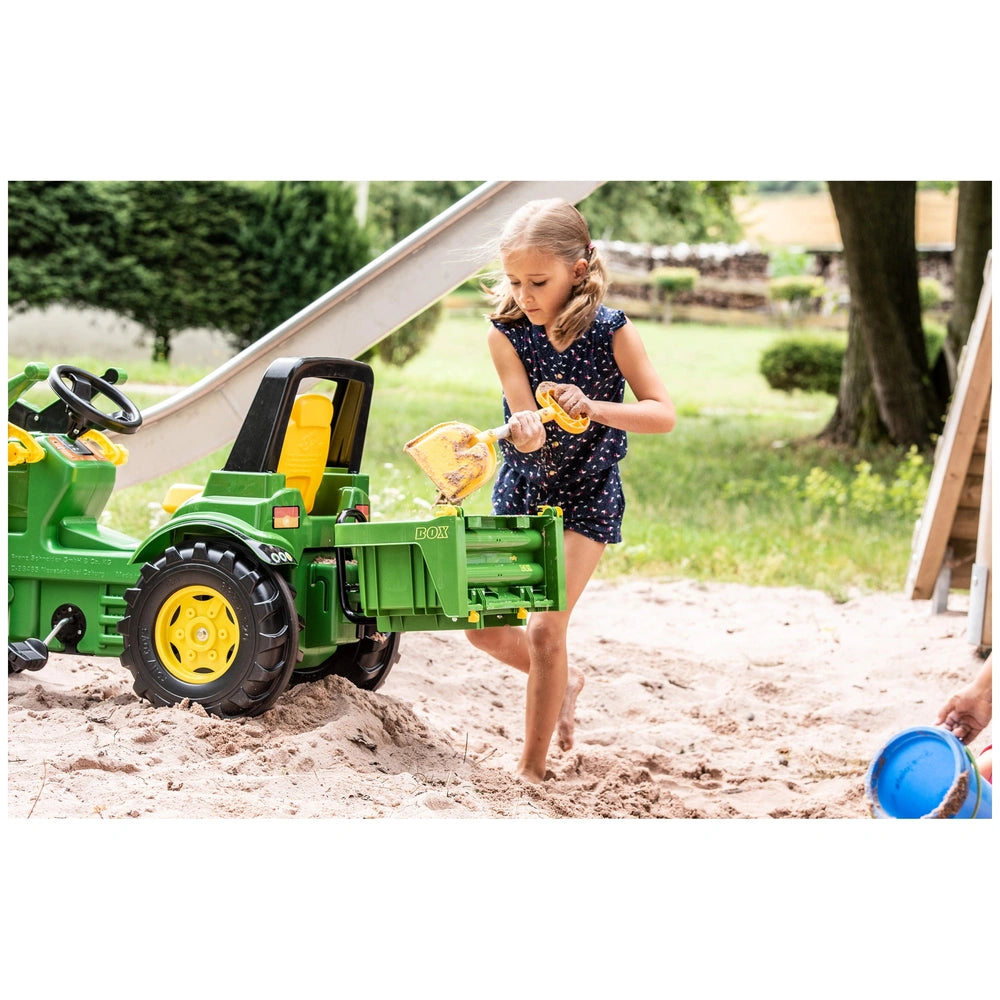 Rollybox John Deere green riding toy with a girl in a blue polka dot dress holding a yellow object, barefoot on grass.