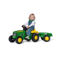 Rolly Toys John Deere tractor with trailer features a smiling toddler in blue overalls and a green scarf, pretending to drive