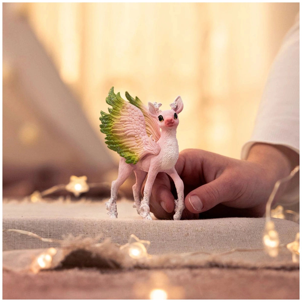 Magical fawn figurine with wings and a soft texture held by a hand in a warm indoor setting.
