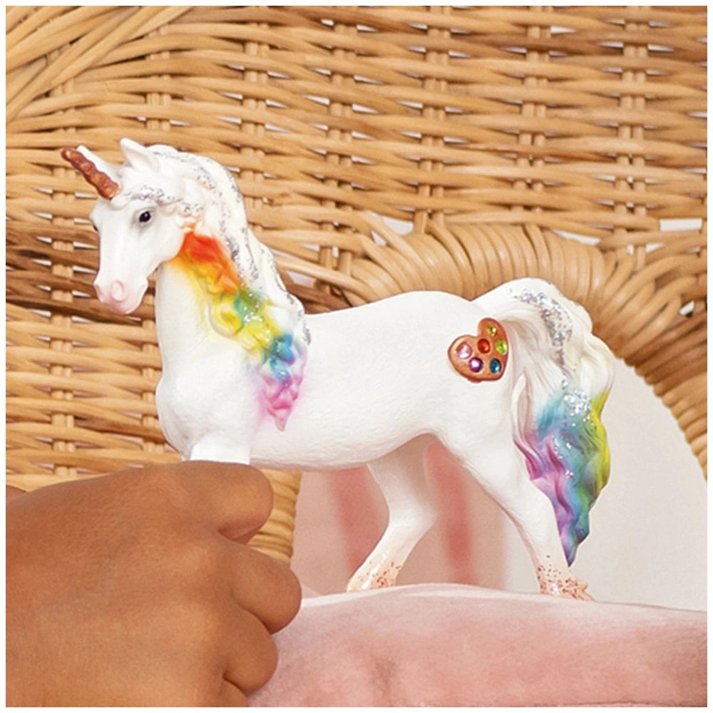 Rainbow Love Unicorn Mare figurine held in a hand, featuring a white body, rainbow mane, and heart-shaped jewel on its forehe