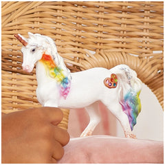 Rainbow Love Unicorn Mare figurine held in a hand, featuring a white body, rainbow mane, and heart-shaped jewel on its forehe