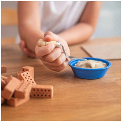Teifoc construction kit with a wooden object held over a blue bowl in a casual indoor crafting environment.