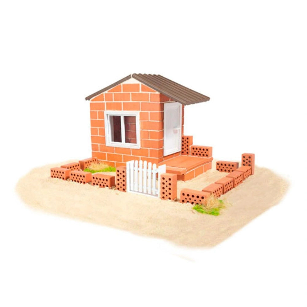 Teifoc beach house model made of Lego bricks in orange, brown, and white, set on a sandy surface with a picket fence.