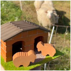 Teifoc sheepfold set features a model house with a chimney, surrounded by grass and a white sheep behind a wire fence.
