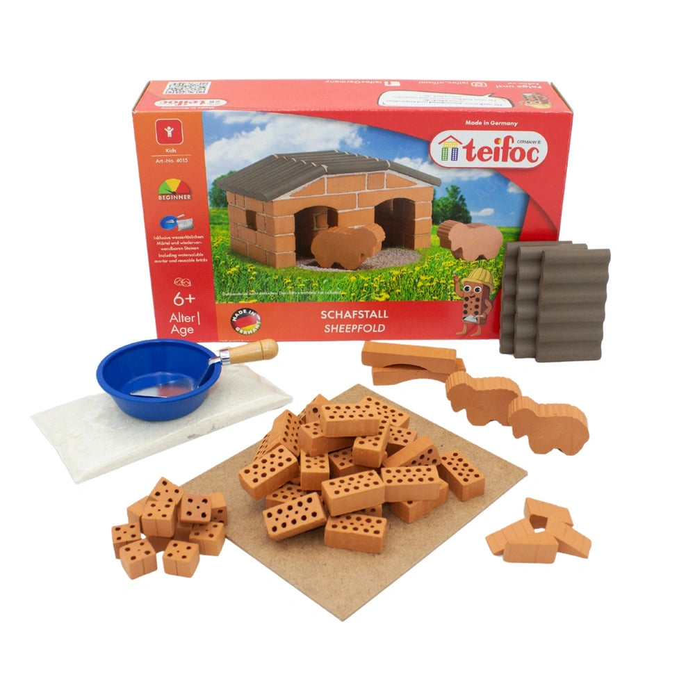 Teifoc Sheepfold construction set includes wooden pieces, a mallet, and a bowl, all displayed in a red box with a cartoon she