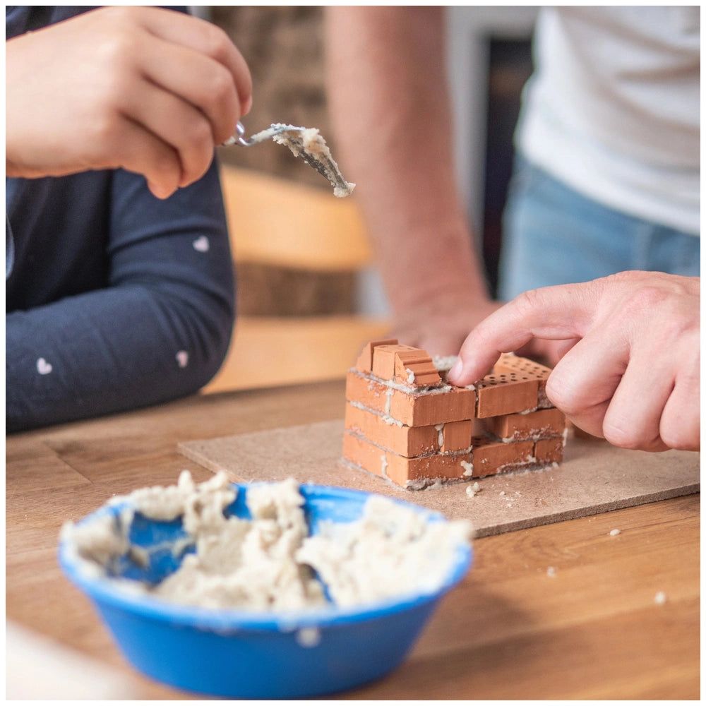 Teifoc small family home set features a person building with colorful Lego bricks and a blue bowl of adhesive on a wooden tab