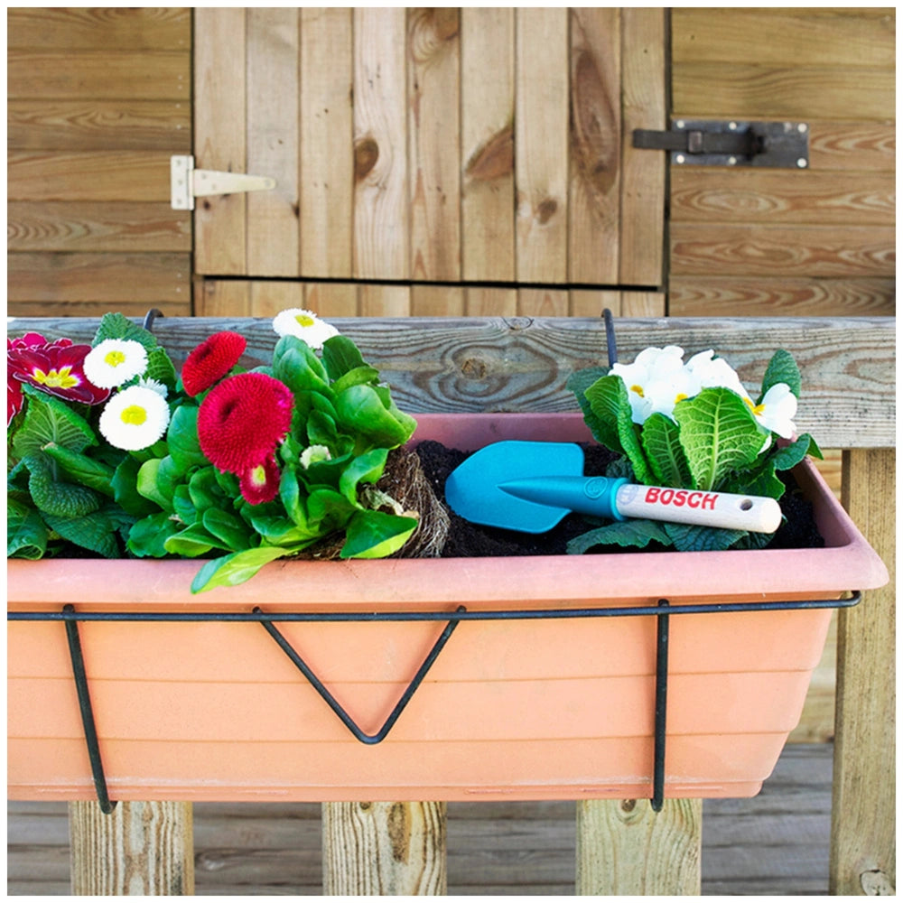 Theo Klein Bosch Garden hand shovel on an orange planter filled with red and white flowers and green leaves.