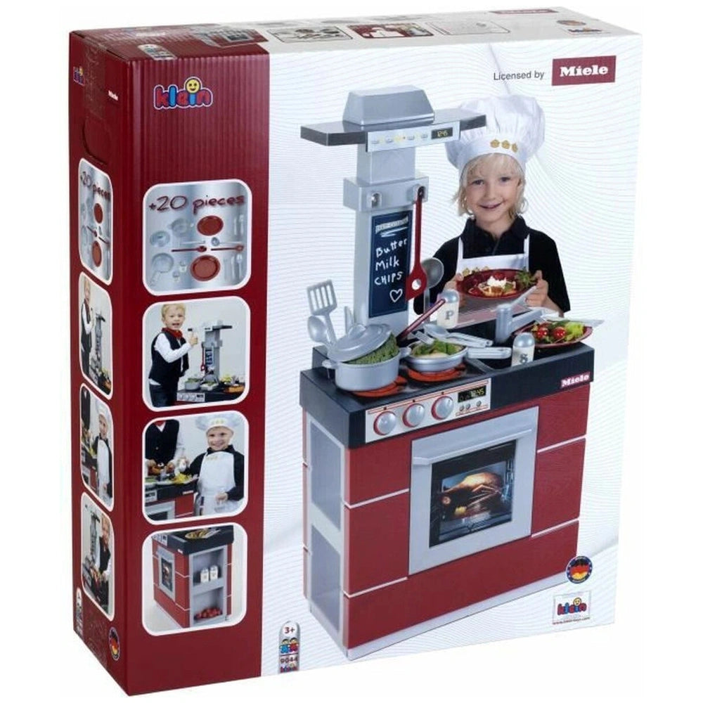 Theo Klein Miele Kitchen Compact toy set with a child in a chef's hat, holding food in front of a black and red toy kitchen.