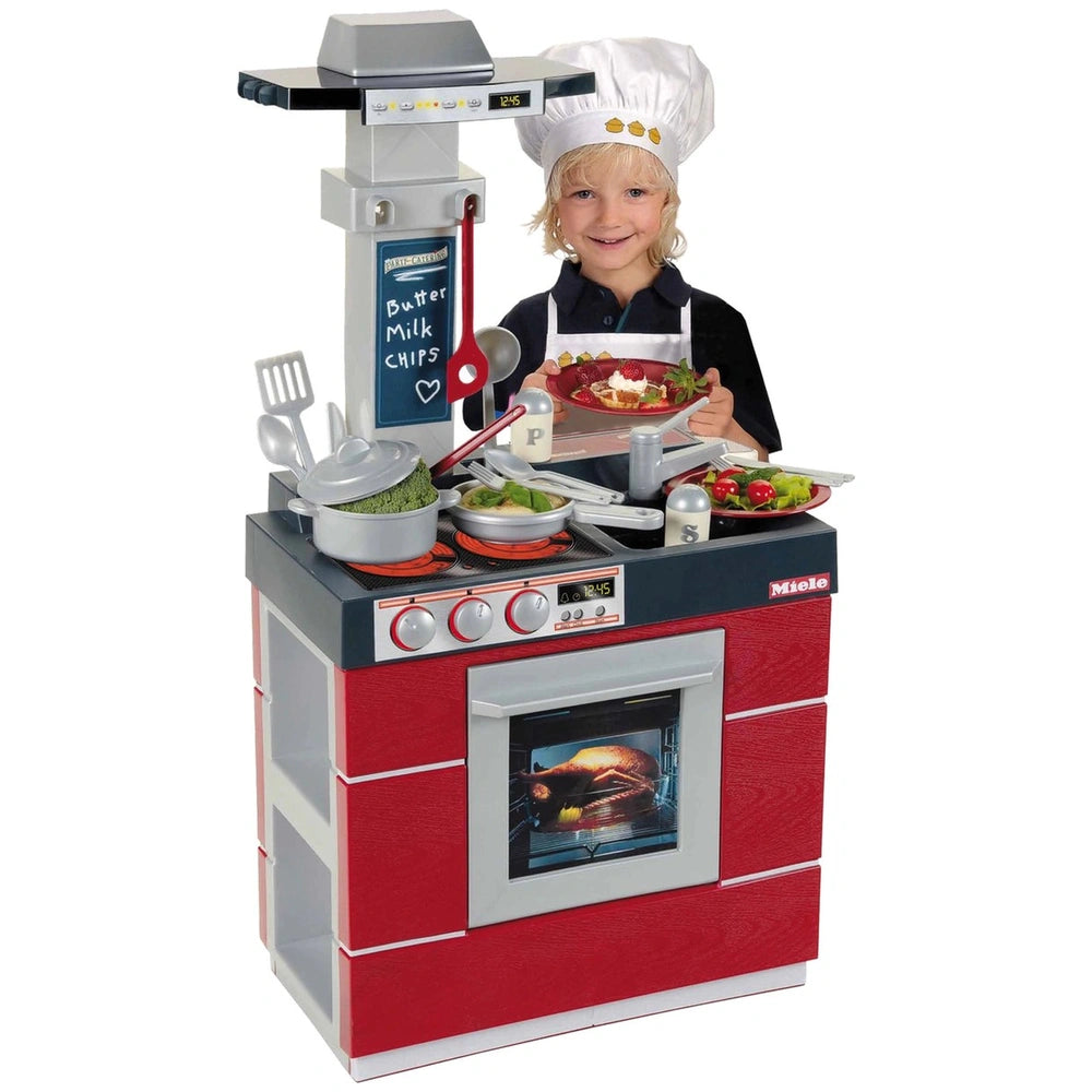 Theo Klein Miele toy kitchen with a child in a chef's hat, holding a plate of food in front of colorful appliances and utensi